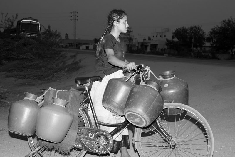 Children and Water - An adolescent girl returning home with partially filled containers at dusk in Anantpur town, Andhra Pradesh